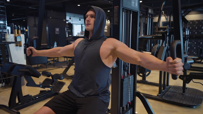Athletic Young Well-built Man Trains Chest Doing Machine Chest Fly Exercise in Gym