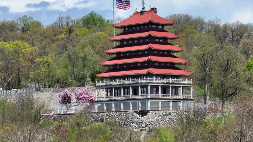 Waving american flag on Pagoda Building in Reading, PA. Top of Mount Penn with forest trees in backdrop. Rising drone wide shot.