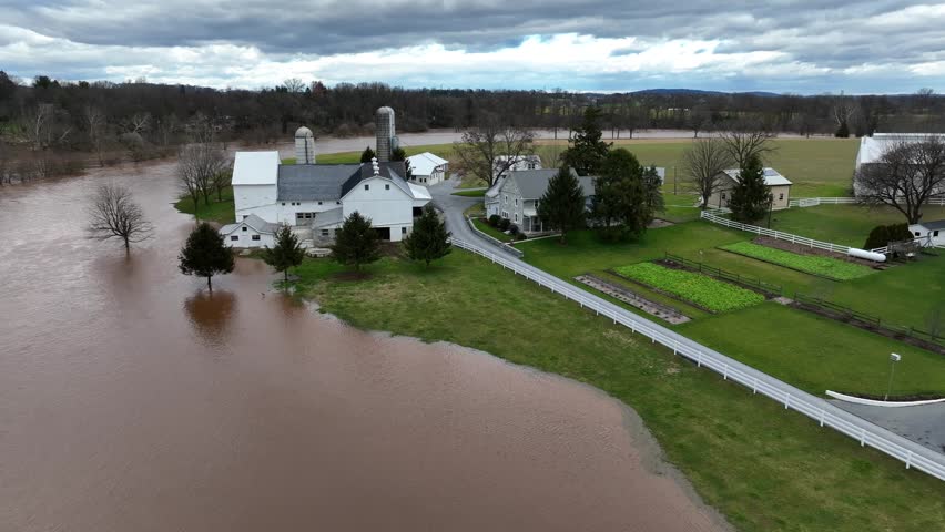 Flooded River at industrial farm with silo and stable in american town. Heavy rain at night destroying farmstead in USA. Dirty water flooding countryside fields. Aerial view.