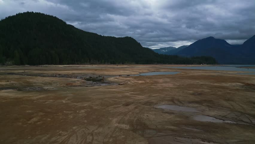 High-angle aerial over Stave Lake mudflats moving swiftly forward tilted straight ahead desolate landscape Dark green mountains backdrop under evening sky isolation solitude, beauty, peacefulness