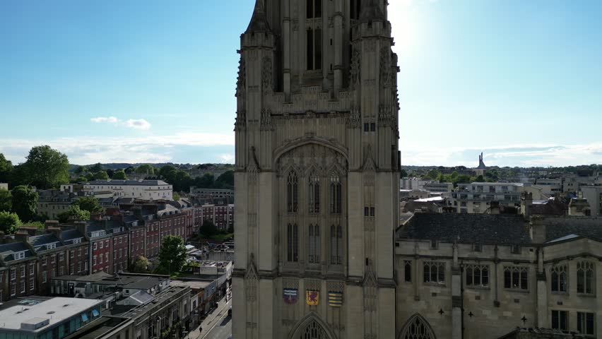 An ascending drone shot of Wills Memorial Building Tower with the sun flare in the dusk sky in the background at sunset in Bristol, England, UK