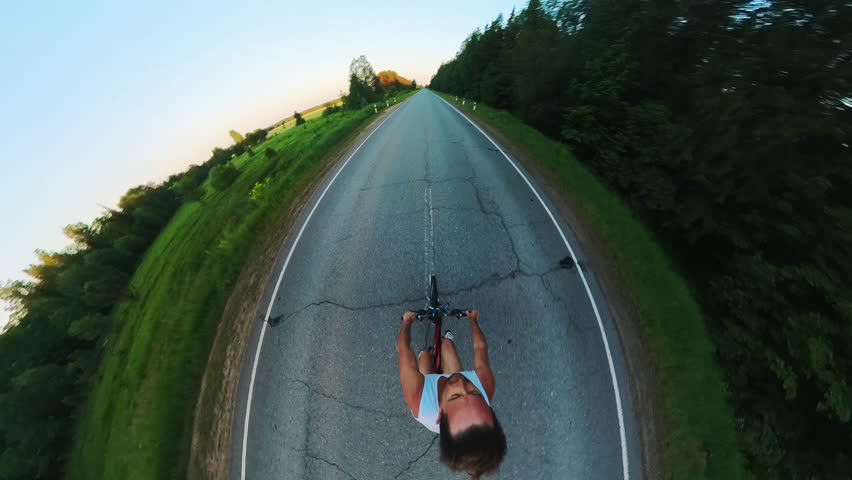 Young man cycling on the asphalt empty road at sunset. Extreme wide angle