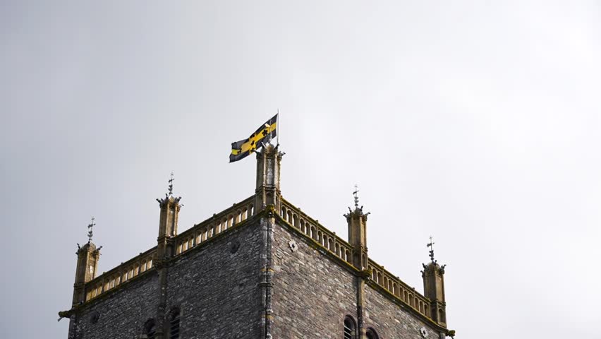 St Davids flag waving in the wind from the top of St Davids Cathedral against a gray sky, Wales