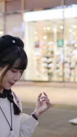 Vertical video of a young and cute Taiwanese woman in her 20s walking and strolling amidst beautiful illuminations at night in a high-end shopping mall area of Xinyi District, Taipei, Taiwan
