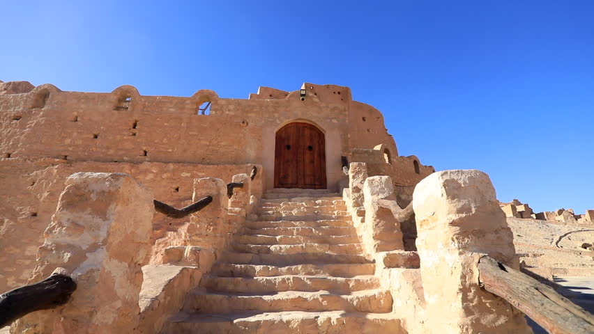 Ancient stone steps lead to a grand wooden door under a bright blue sky in Tunisia