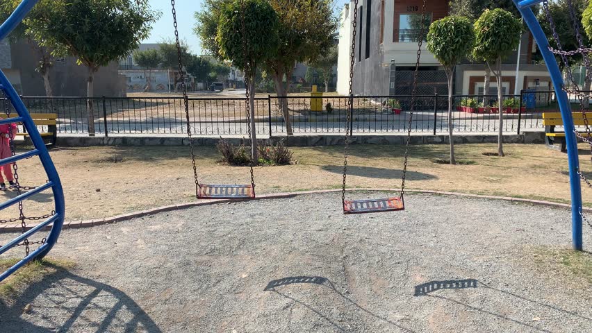 Two empty swings swinging in a playground on a sunny day in Bahria Enclave, Islamabad, Pakistan