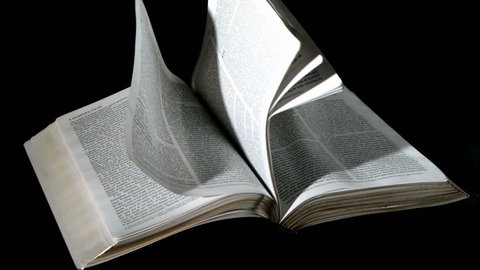 Bible pages turning in the wind on black background in slow motion