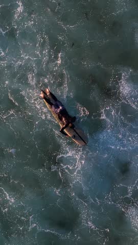 A slow motion vertical drone footage of a surfer on surfboard trying to catch a wave at Maroubra Beach in Sydney, New South Wales, Australia