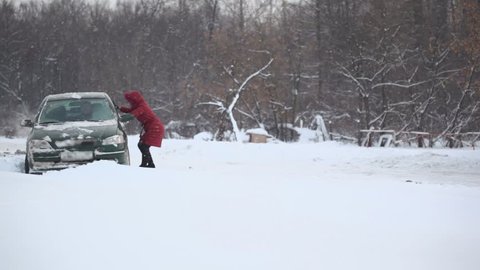Woman helps to release car from snow trap on country road at winter day