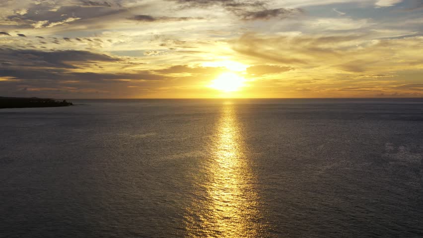 Stunning golden sunset over the Hawaiian ocean, casting a brilliant reflection on the water and illuminating the sky.
