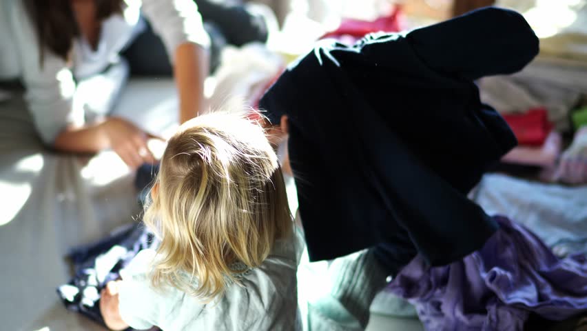 Little girl plays with her mother among a pile of laundry on the bed