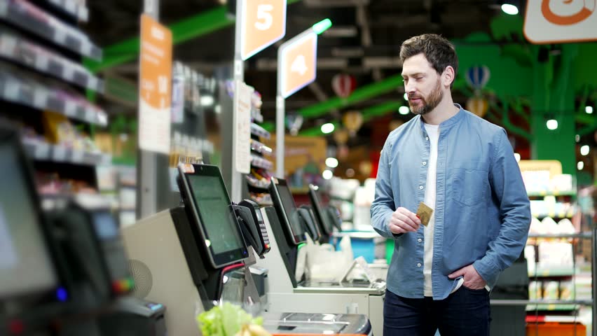 Male customer using a self-service cashier checkout in a supermarket. Shopper scanning produce items using at grocery store self serve cash register. cashier terminal man pay for products online
