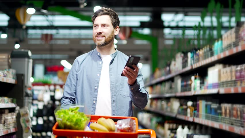 Handsome middle aged man buyer customer checking shopping list using smartphone, purchasing in grocery store in supermarket male shopper pick use mobile phone in hypermarket or food market deli