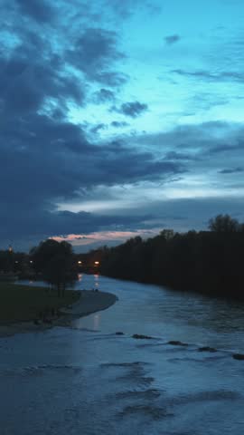 Munich at dramatic dusk sunset. View of Isar river, trees and St Maximilian church from Reichenbach Bridge in Autumn. Munchen, Bavaria, Germany. Camera horizontal pan