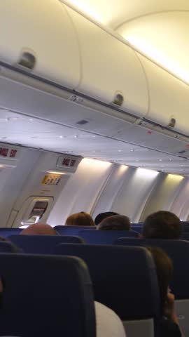 Passengers sits on seats aircraft while flying. Stewardess inside cabin of commercial plane while flight. Air traveling by commercial airplane. Economy class