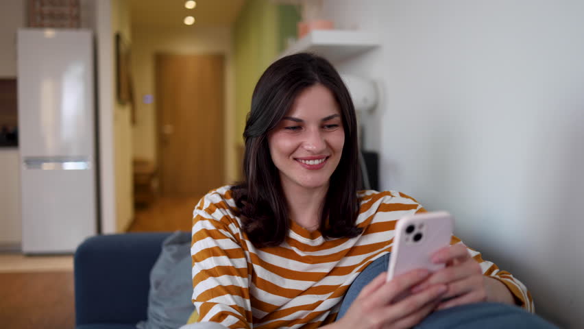 Satisfied woman enjoying her home life and using smartphone