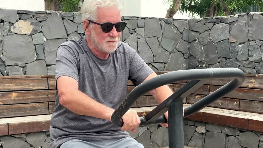 Attractive smiling retired man exercising outdoors with sports free equipment to keep fit. Cardio and muscle exercises for mature people. Athletic spirit concept