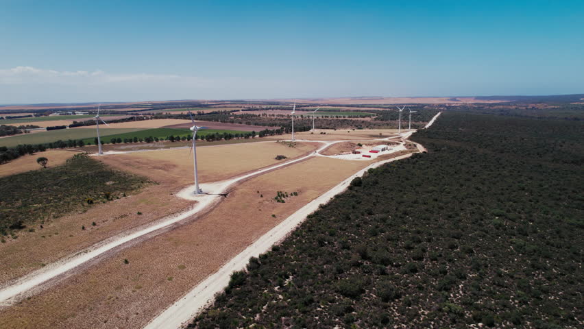A dusty road leads towards a row of wind turbines set against a blue sky in rural Australia.