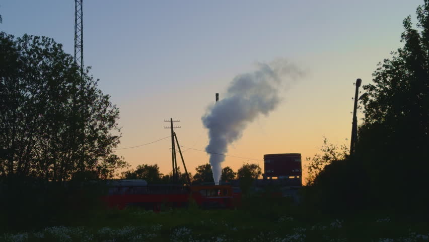 Smoke coming from diesel locomotive in golden twilight. Dark silhouettes of trees and electric poles on railway station. Transportation of heavy shipment by coal loco train using railroad. Transport