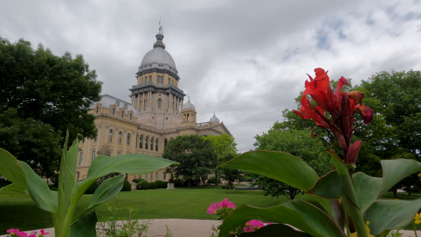 Views of the Illinois State Capitol Building in Springfield, IL, USA as viewed through a blooming floral garden. Dramatic cloudscape and green leafy trees surround the scene.