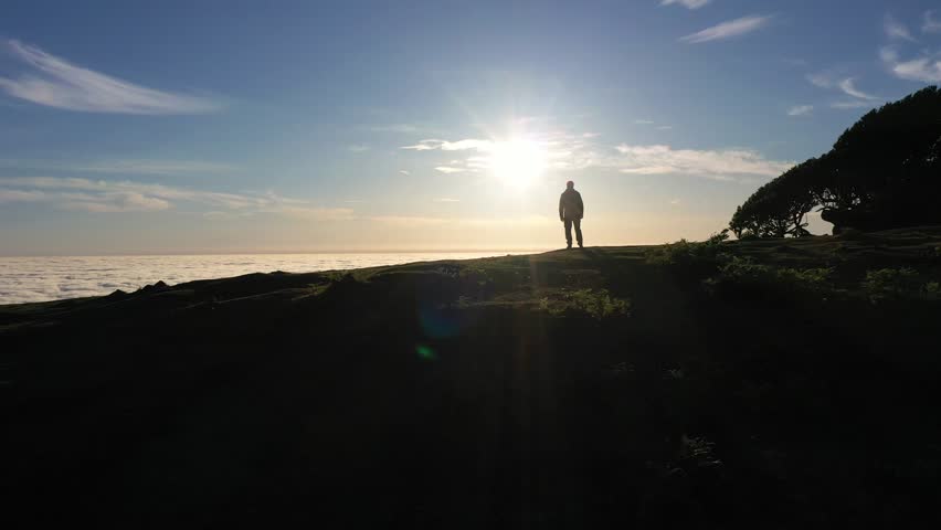 Silhouette of Man on Hill Looking at Sunrise. Clouds Inversion. Aerial Drone Shot. Madeira, Portugal. Moving Forward and Upwards. Reveal Shot
