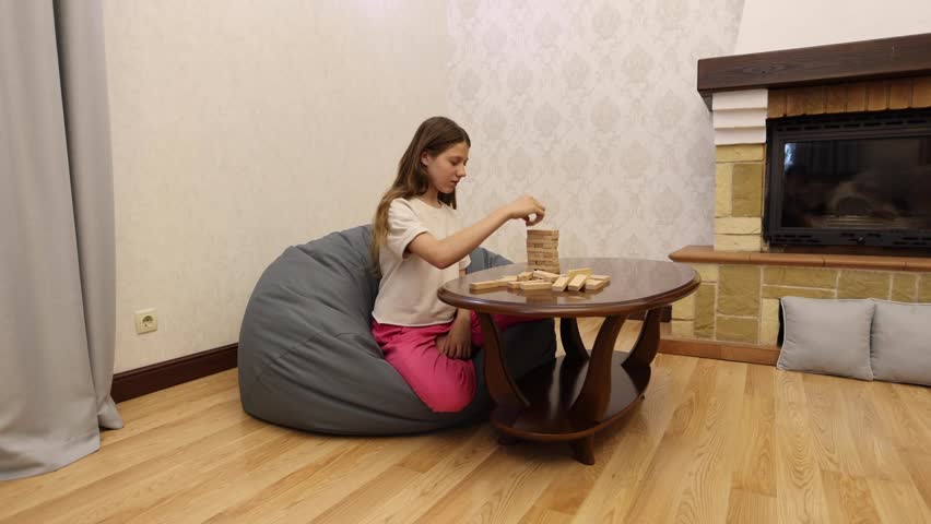 A young woman sits in a beanbag chair and plays a board game at a table with a fireplace in the background