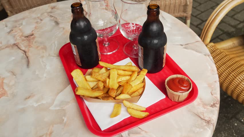 Belgian fries with ketchup and Belgian bottled beer stand on a table on the summer terrace in a street cafe. Traditional Belgian dish