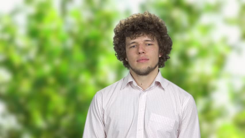 Happy young man with curly hair dreaming outdoors. Tree leaves in the background.