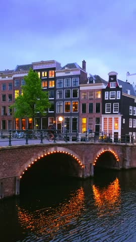 Night view of Amsterdam cityscape with canal, bridge and medieval houses in the evening twilight illuminated. Amsterdam, Netherlands