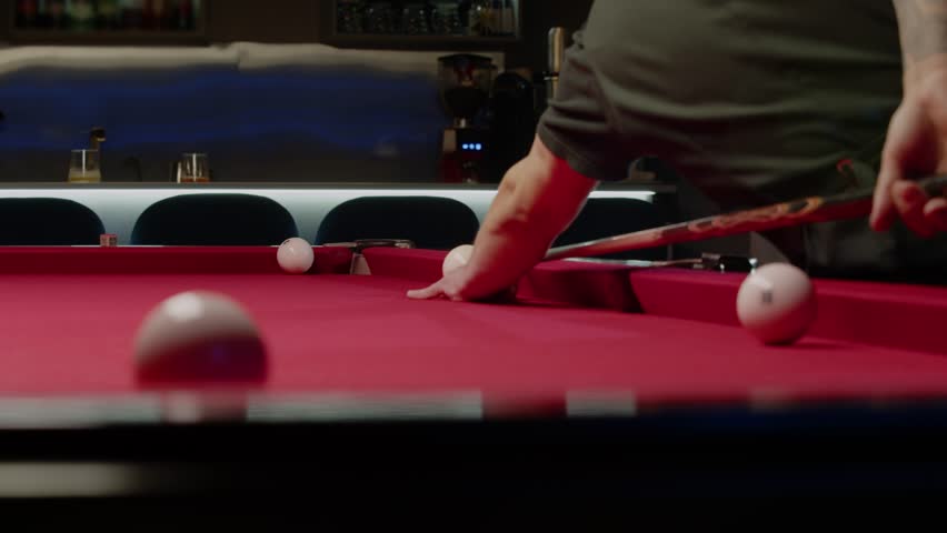 Professional billiards player expertly pockets a ball from an unusual position. The billiard cue is behind him. Medium shot. Slow motion