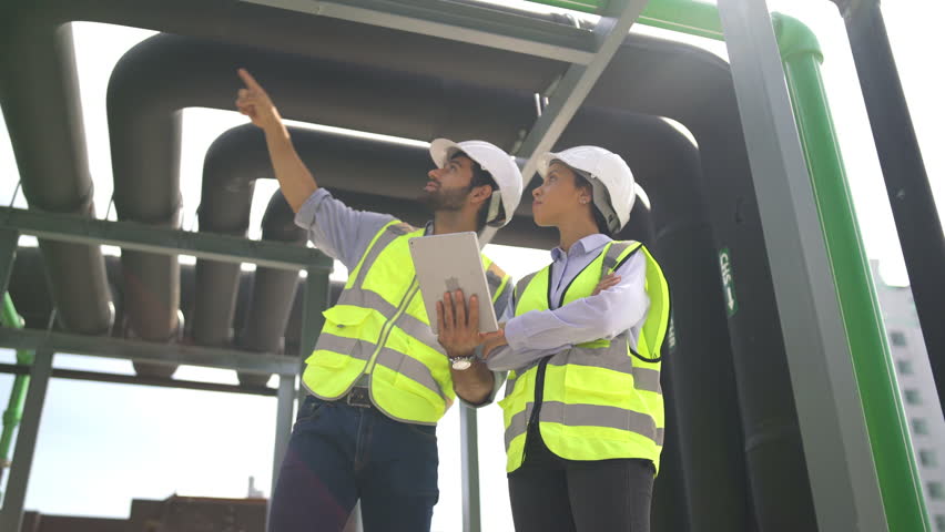 Professional engineer discuss with tablet about construction site and stay under the floating pipe or pipe hanging on deck of building.