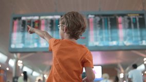 Little boy points to something at the airport. Departures information board is visible in background. Traveling with child. Family vacation. Flying with kid. - Powered by Shutterstock - Get 15% off with code: PIKWIZARD15