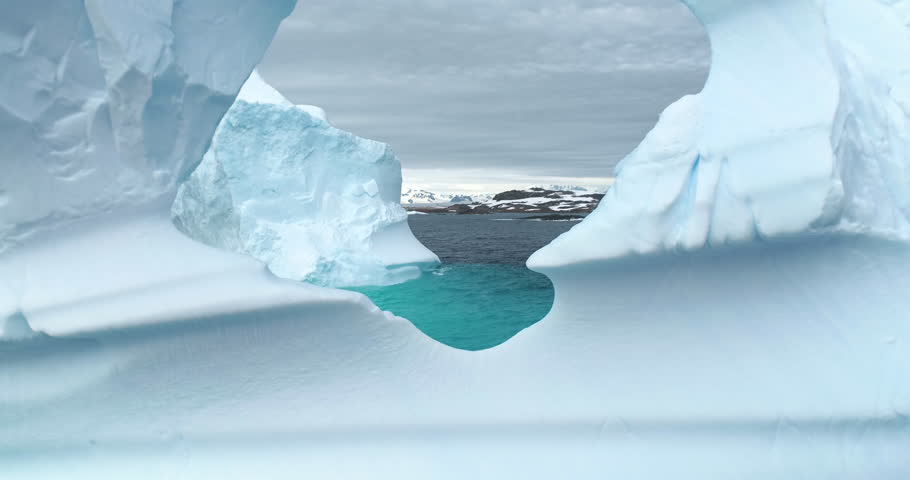 Cracked hole in melting iceberg in Antarctica ocean close up. Drone fly inside frozen glacier cave arch window drifting blue cold water. Arctic winter landscape, global warming. Polar climate change