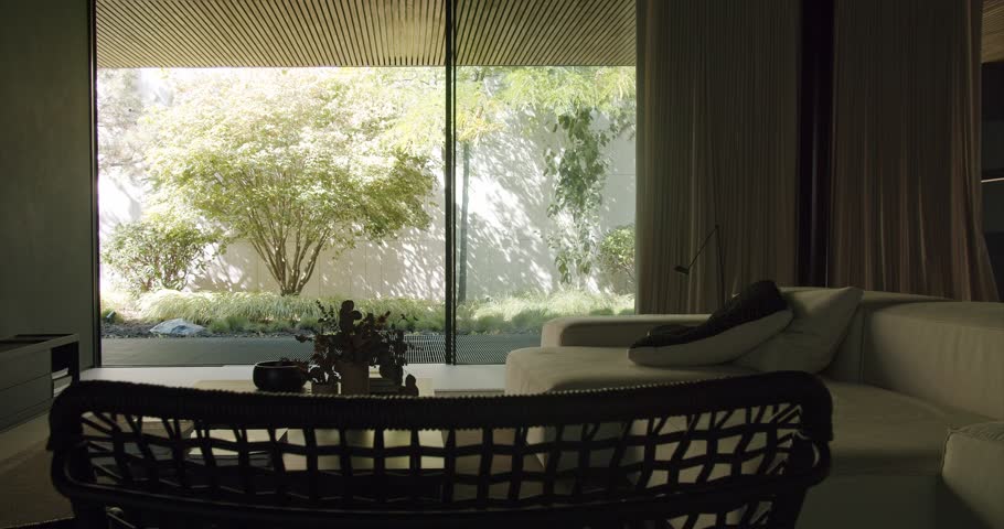 A tranquil home interior scene showcasing a stylish living area bathed in natural light with a panoramic view of a lush green garden and serene trees through a large glass window. Modern Home Interior