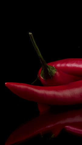 Hot red chili peppers in flames on a black background. Spicy food concept. Close-up, vertical footage