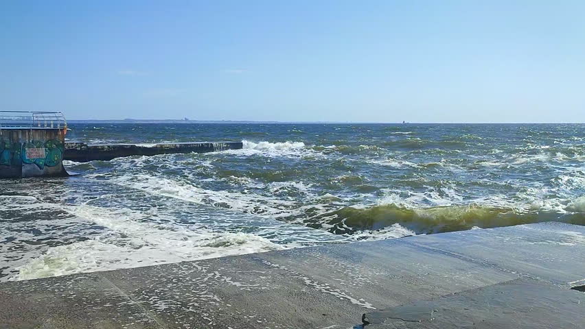Storm. Storm at sea. Large high sea waves with white foam hitting concrete pier wall and splashing on hot sunny summer day. Stormy sea weather. Rough sea. Shore and waves. Nature. Natural background