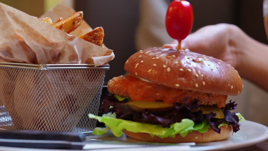 Boy eating tasty chicken burger with side of crispy fries in basket served on white plate in restaurant. Fast food and junk food concept