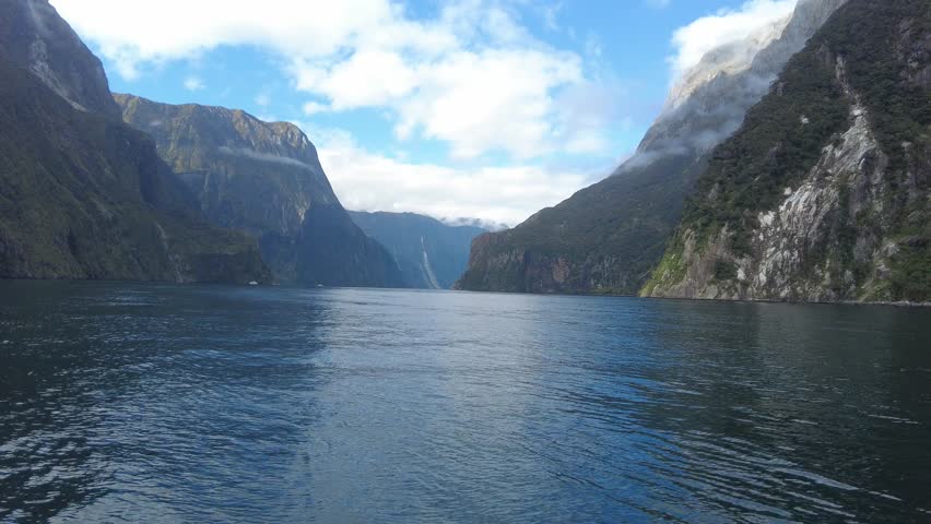 Drone flight over the stunning waters of Milford Sound, New Zealand, capturing breathtaking views of the fjord's towering cliffs and lush rainforests.