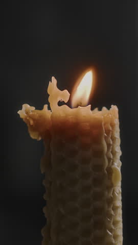 Vertical close-up shot of wax candle burning on dark background