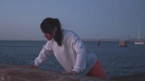 Determined sporty woman doing push ups while leaning on retaining wall by sea against clear sky at dusk. Fit young woman is doing strength exercises in nature.  - Powered by Shutterstock - Get 15% off with code: PIKWIZARD15