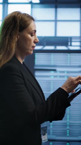 Vertical video Technician doing checkup using tablet to prolong data center electronics life span and avoid downtime. Employee walking in server room, monitoring server infrastructure using digital