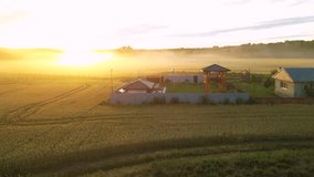 High angle shot of golden sunset on a wheat field with tiny villas around it. Fog and mist seen from a drone. Flying footage of beautiful rural landscape on a summer evening. Playground in the fields. - Powered by Shutterstock - Get 15% off with code: PIKWIZARD15