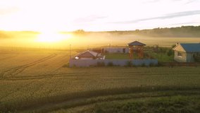 High angle shot of golden sunset on a wheat field with tiny villas around it. Fog and mist seen from a drone. Flying footage of beautiful rural landscape on a summer evening. Playground in the fields. - Powered by Shutterstock - Get 15% off with code: PIKWIZARD15