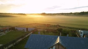 High angle shot of golden sunset on a wheat field with tiny villas around it. Fog and mist seen from a drone. Flying footage of beautiful rural landscape on a summer evening. Playground in the fields. - Powered by Shutterstock - Get 15% off with code: PIKWIZARD15