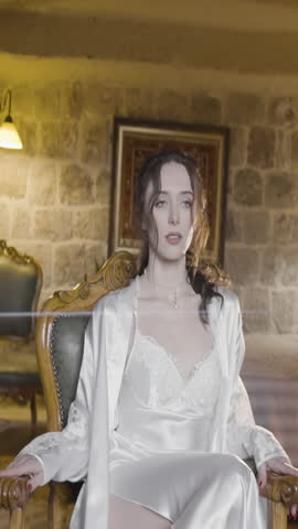 Morning of a bride. Action. Beautiful bride in a hotel room in a white silk nightdress with a wedding dress behind her.