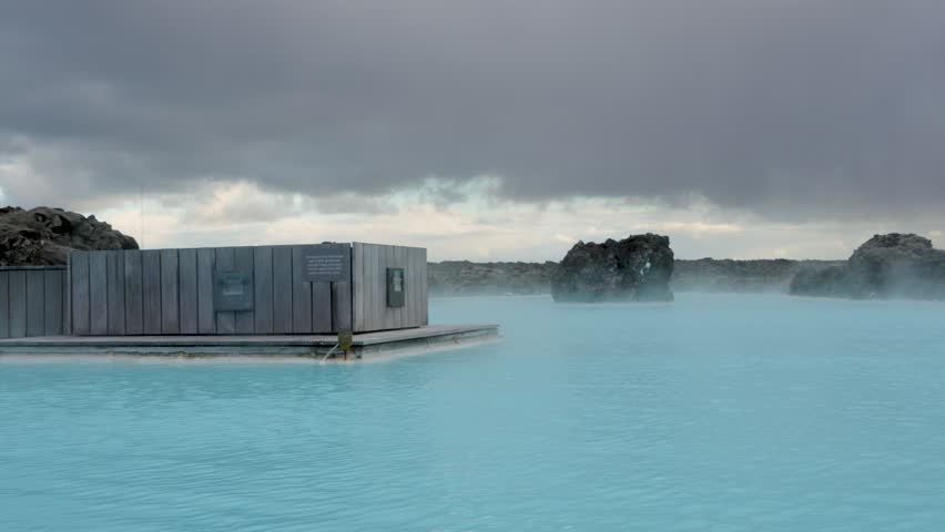 Milky blue waters of the Blue Lagoon in Iceland contrast with black lava rocks and lichen; a peaceful geothermal spa scene. Reykjanes Peninsula, Iceland.