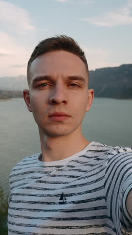 Young hiker traveler man taking selfie at mountain top. Action. Young happy man with mountains and beautiful lake on the background.
