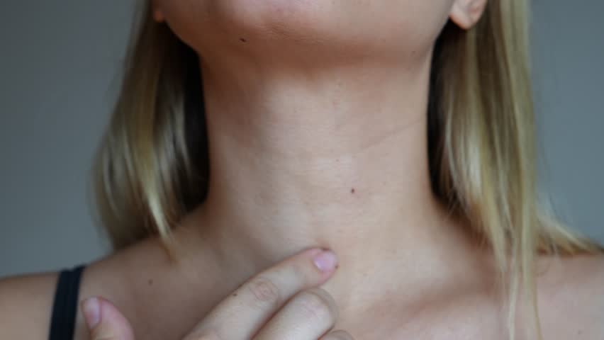 Young blonde woman touching her neck with her hands on a grey background. Lines on the female neck. Wrinkles, age-related changes, rings of Venus, creases, goosebumps