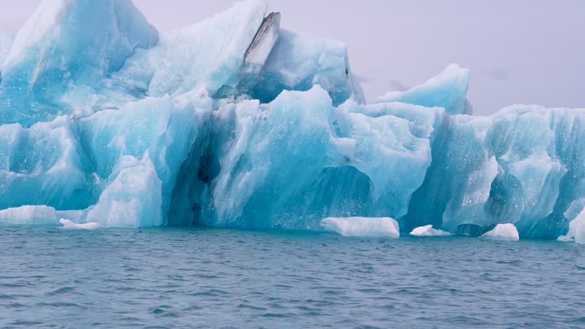 Blue and white icebergs float in a glacial lake against a backdrop of glaciers, creating a serene scene. Unspoiled Jokulsarlon, Iceland.