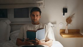 Man reading book in bedroom feeling serene and relaxed mood at night closeup. Engaged male reader absorbed in literature at lamp light. Calm guy enjoy hobby lying bed in tranquil home atmosphere. - Powered by Shutterstock - Get 15% off with code: PIKWIZARD15